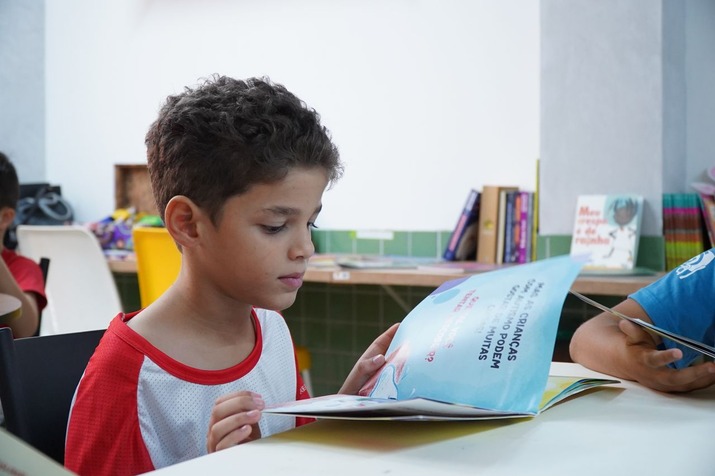 Young boy in a classroom reading a book at a table.