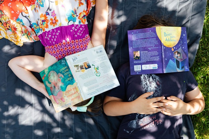 Two kids lying on grass with books covering their faces.